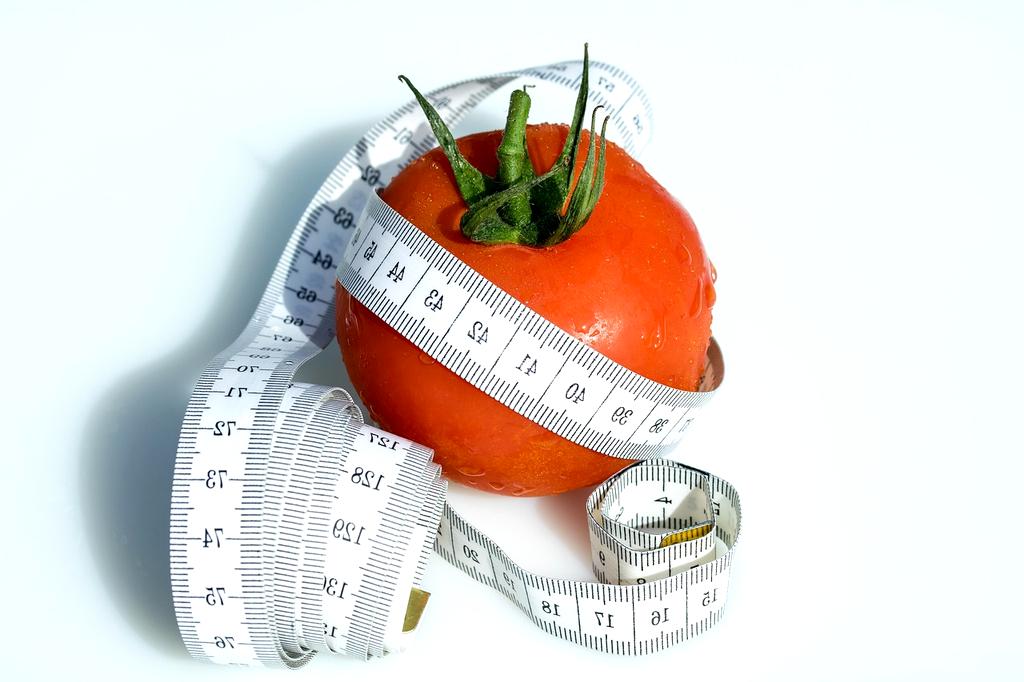 Glass of water with lemon beside a measuring tape on a white surface