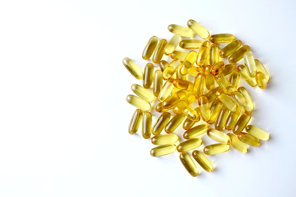 Glass of omega-3 fish oil softgel supplements with lemons